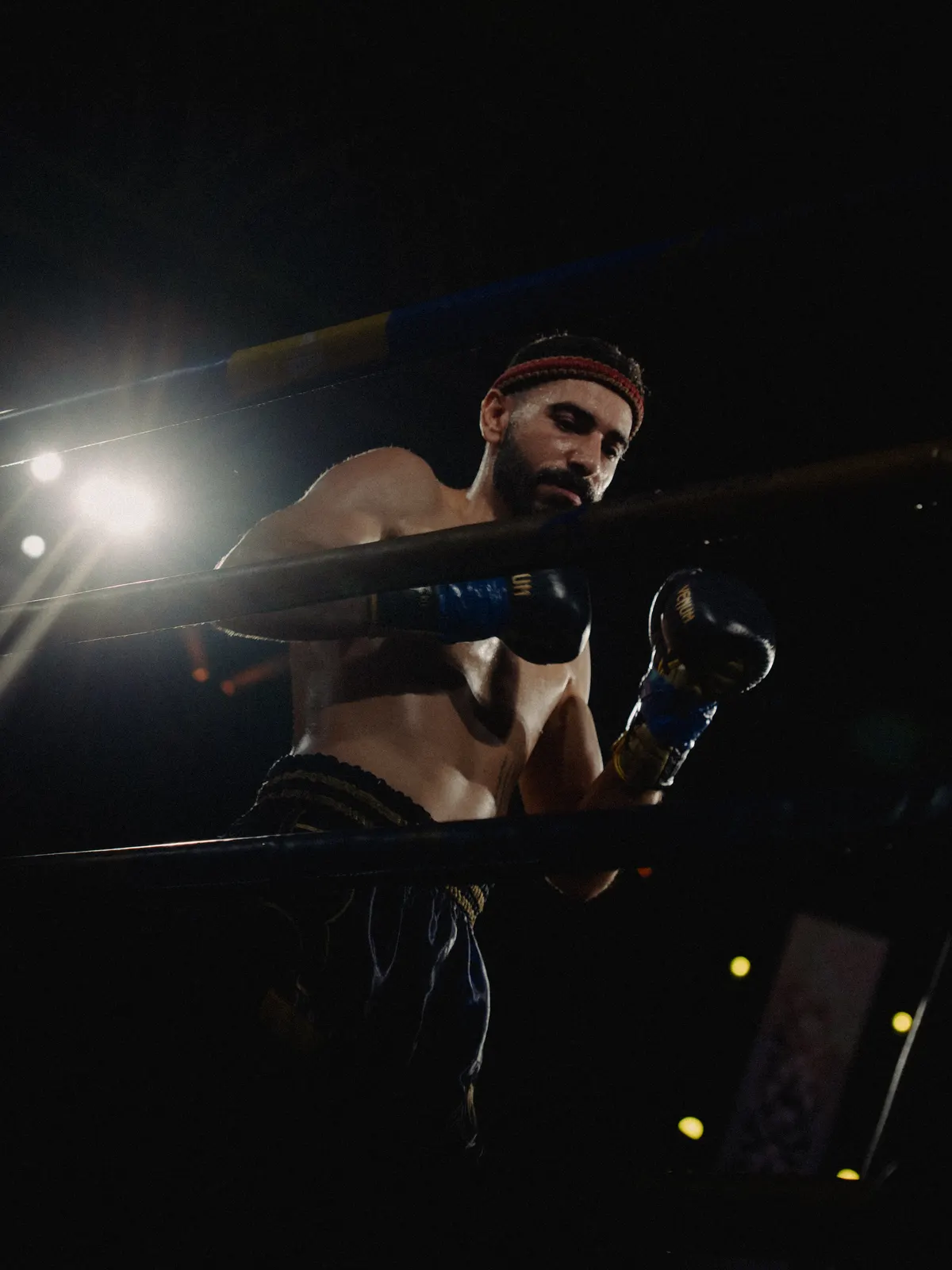 A Stubborns fighter in the ring corner under the lights, gloves up between rounds