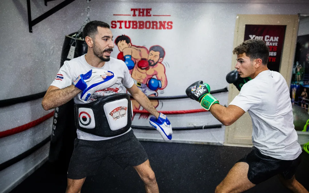 A Stubborns coach in a belly pad and focus mitts working combinations with a member inside the ring