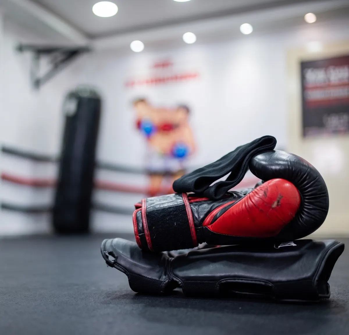 Kickboxing gloves and shin guards resting on the ring floor at The Stubborns